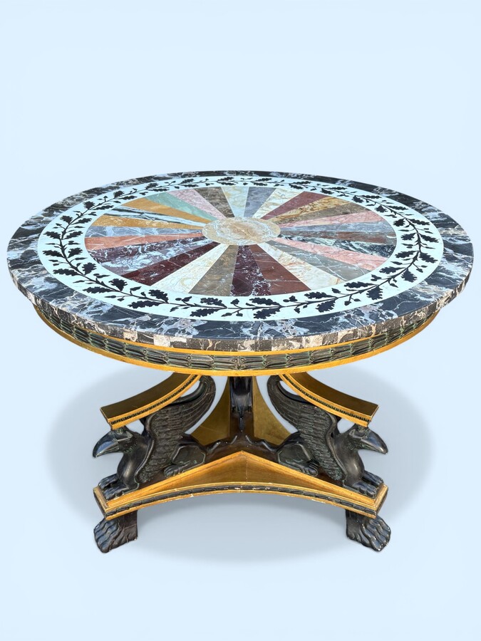 A lovely Empire-style center table, 1830–1840 A highly decorative center table in patinated and gilded wood, comprising a three-legged base adorned with three reclining winged mythological creatures and a suspended gilded wooden sphere