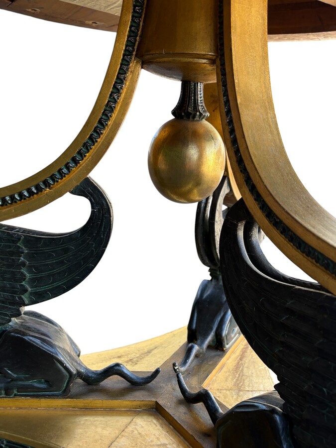 A lovely Empire-style center table, 1830–1840 A highly decorative center table in patinated and gilded wood, comprising a three-legged base adorned with three reclining winged mythological creatures and a suspended gilded wooden sphere