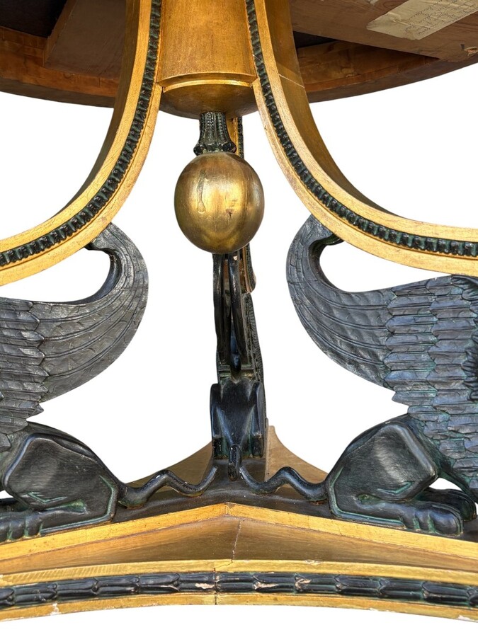 A lovely Empire-style center table, 1830–1840 A highly decorative center table in patinated and gilded wood, comprising a three-legged base adorned with three reclining winged mythological creatures and a suspended gilded wooden sphere