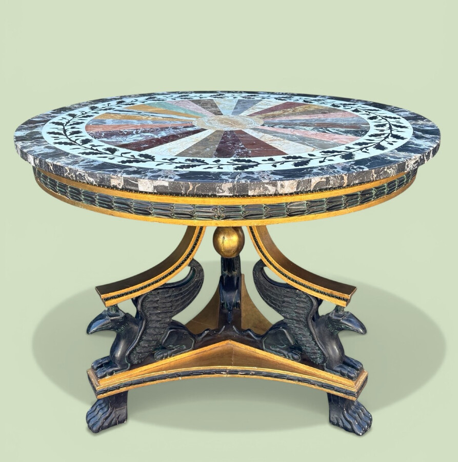 A lovely Empire-style center table, 1830–1840 A highly decorative center table in patinated and gilded wood, comprising a three-legged base adorned with three reclining winged mythological creatures and a suspended gilded wooden sphere