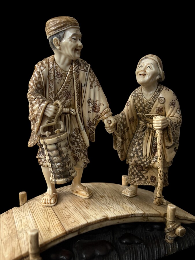 A nice ivory sculpture, China, 19th century An ivory sculpture with very fine detail depicting an elderly couple in kimonos walking across a bridge over water The water beneath the bridge is carved from wood. Dimensions: Width: 17 cm Height: 18 cm