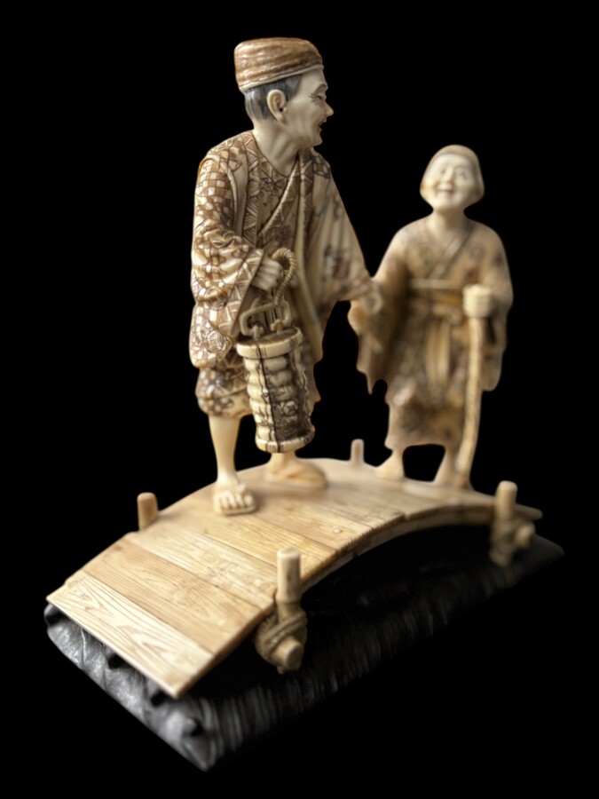 A nice ivory sculpture, China, 19th century An ivory sculpture with very fine detail depicting an elderly couple in kimonos walking across a bridge over water The water beneath the bridge is carved from wood. Dimensions: Width: 17 cm Height: 18 cm