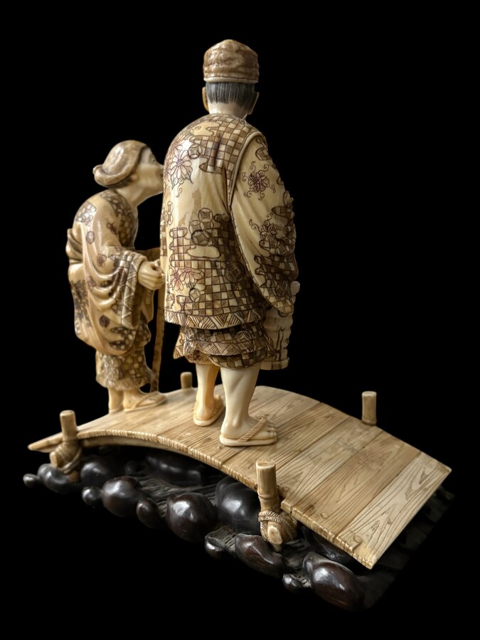 A nice ivory sculpture, China, 19th century An ivory sculpture with very fine detail depicting an elderly couple in kimonos walking across a bridge over water The water beneath the bridge is carved from wood. Dimensions: Width: 17 cm Height: 18 cm