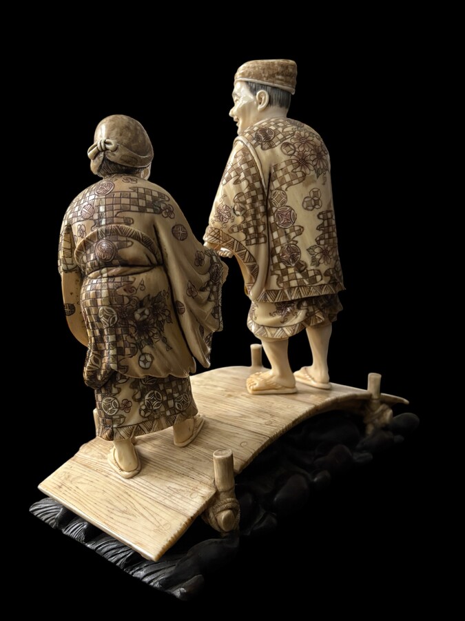 A nice ivory sculpture, China, 19th century An ivory sculpture with very fine detail depicting an elderly couple in kimonos walking across a bridge over water The water beneath the bridge is carved from wood. Dimensions: Width: 17 cm Height: 18 cm