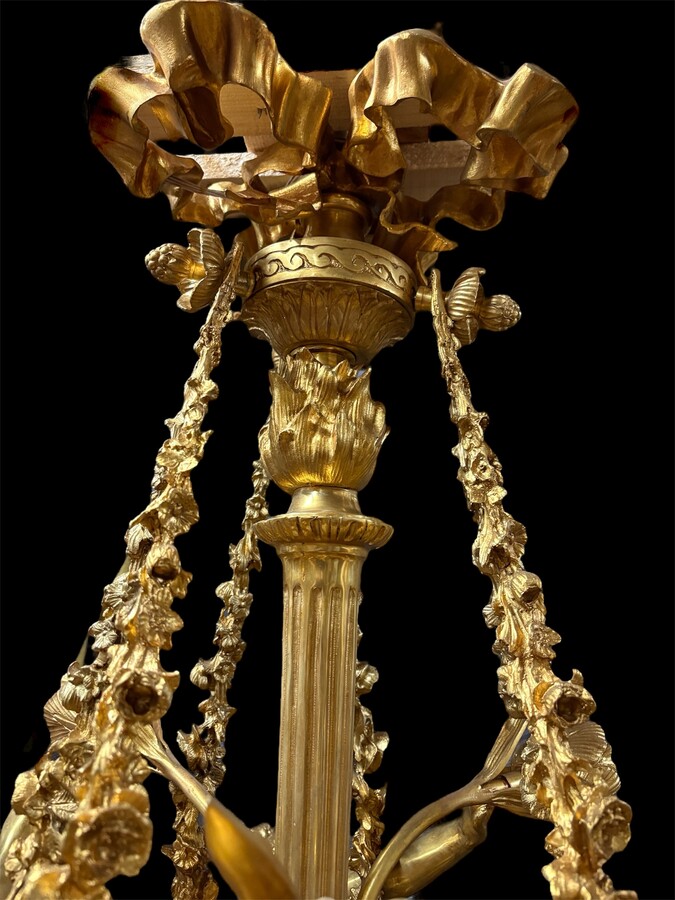 A pair of large gilded bronze chandeliers depicting three mythological women , 20thC. Nice chandeliers with 15 light points, featuring three mythological women holding a bouquet of flowers; at the top, a large Louis XVI-style bow 