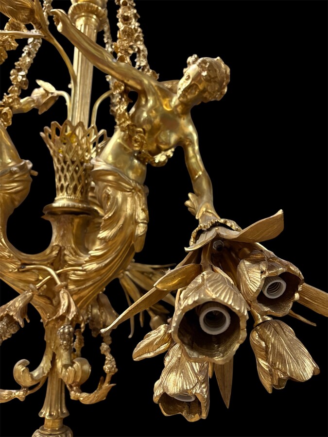 A pair of large gilded bronze chandeliers depicting three mythological women , 20thC. Nice chandeliers with 15 light points, featuring three mythological women holding a bouquet of flowers; at the top, a large Louis XVI-style bow 