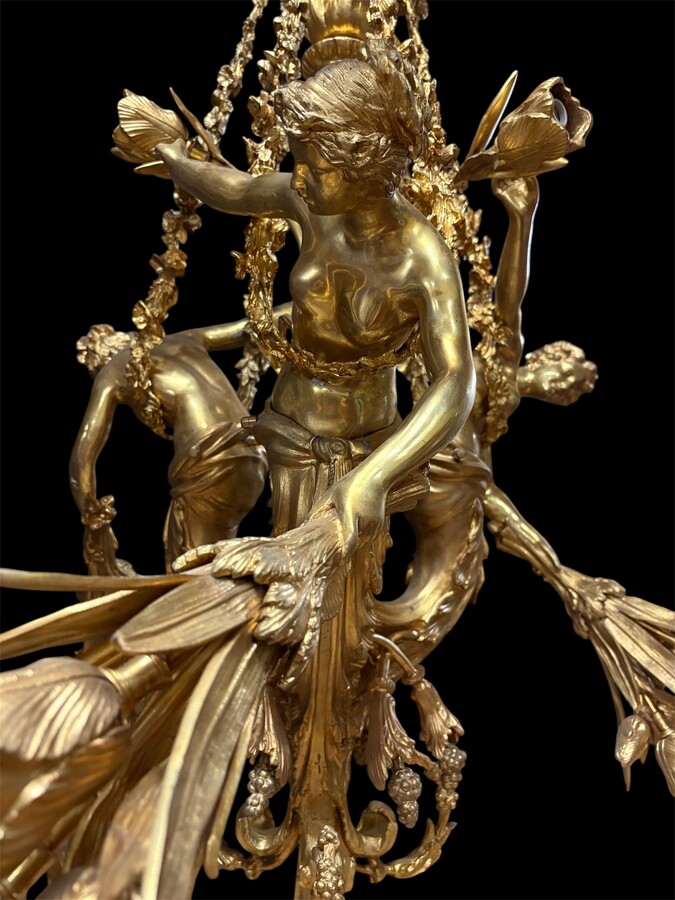 A pair of large gilded bronze chandeliers depicting three mythological women , 20thC. Nice chandeliers with 15 light points, featuring three mythological women holding a bouquet of flowers; at the top, a large Louis XVI-style bow 