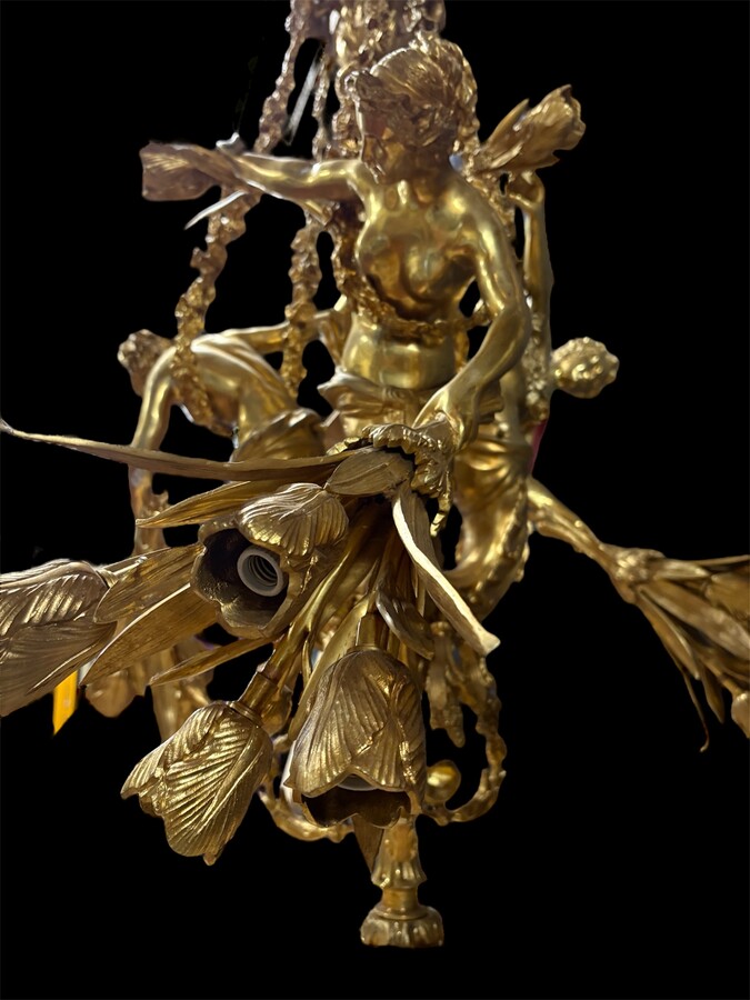 A pair of large gilded bronze chandeliers depicting three mythological women , 20thC. Nice chandeliers with 15 light points, featuring three mythological women holding a bouquet of flowers; at the top, a large Louis XVI-style bow 