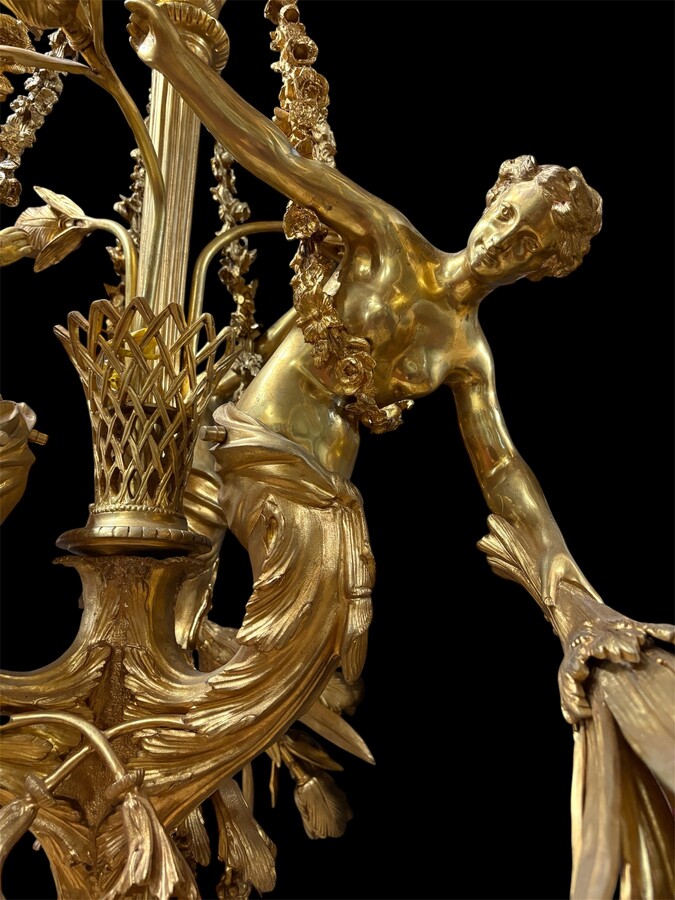 A pair of large gilded bronze chandeliers depicting three mythological women , 20thC. Nice chandeliers with 15 light points, featuring three mythological women holding a bouquet of flowers; at the top, a large Louis XVI-style bow 
