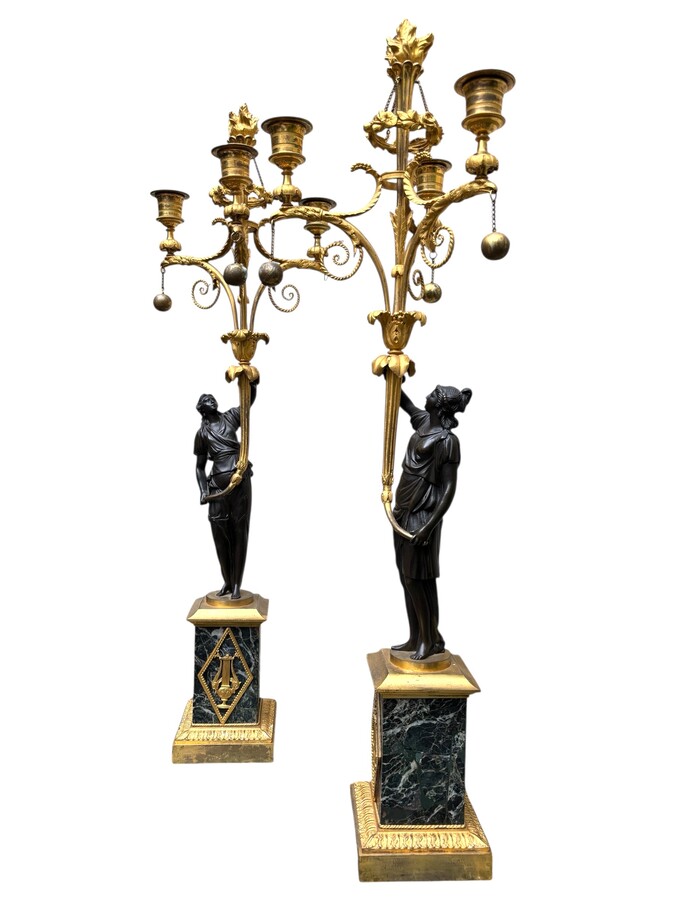 An elegant pair of candelabras in finely chased, gilded and patinated bronze. The shaft is adorned with an antique draped female figure, resting on a green marble base. In the Louis XVI style, these pieces date from the early 19th century. 
