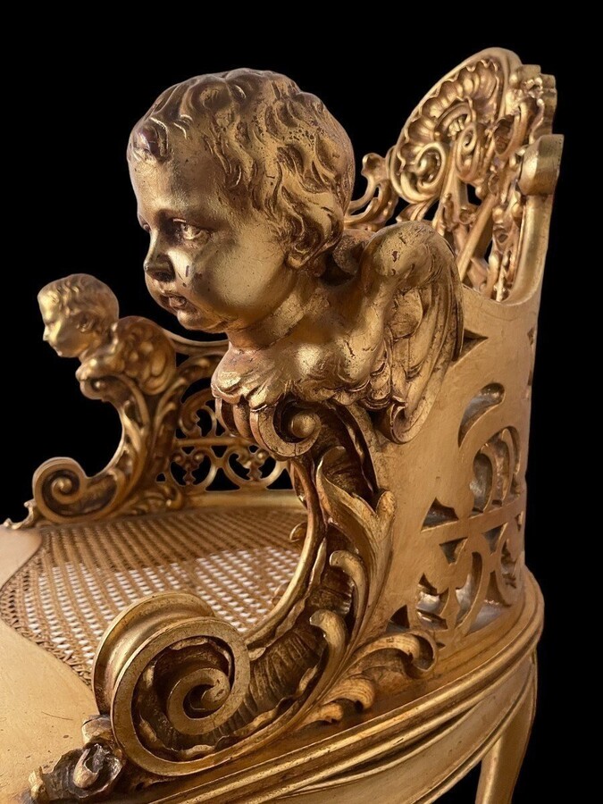 An honorary seat with angel heads in gilt wood 19th century. Special seat decorated with scrolls, ornaments and angel heads in gilt wood. Seat in wicker. Dimensions : Height : 93 cm Width : 71 cm Depth : 58 cm Seat height : 39 cm Decorative chair