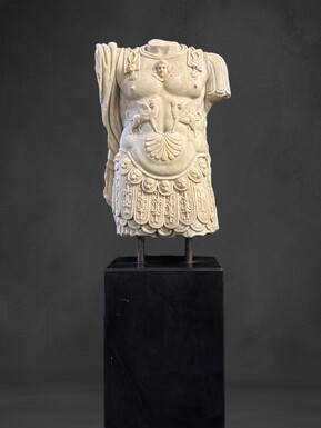 An impressive sculpture of a Roman torso in white marble, exuding the power and beauty of classical antiquity. The detailed breastplate is richly decorated with hand-carved mythological motifs. 