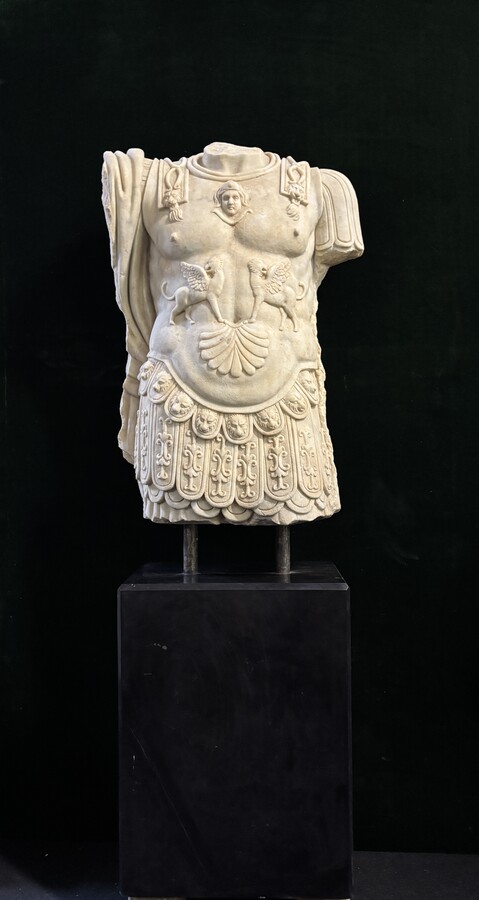 An impressive sculpture of a Roman torso in white marble, exuding the power and beauty of classical antiquity. The detailed breastplate is richly decorated with hand-carved mythological motifs. 