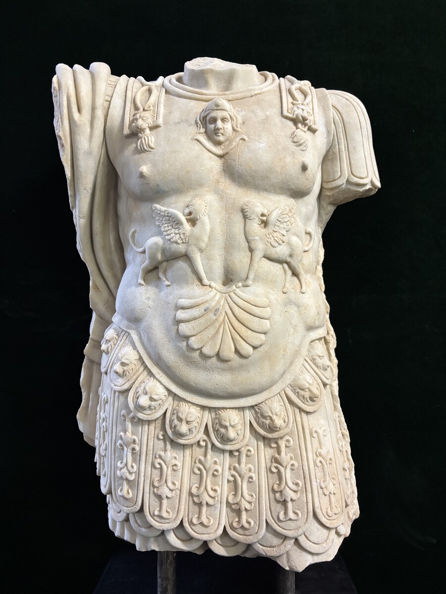 An impressive sculpture of a Roman torso in white marble, exuding the power and beauty of classical antiquity. The detailed breastplate is richly decorated with hand-carved mythological motifs. 
