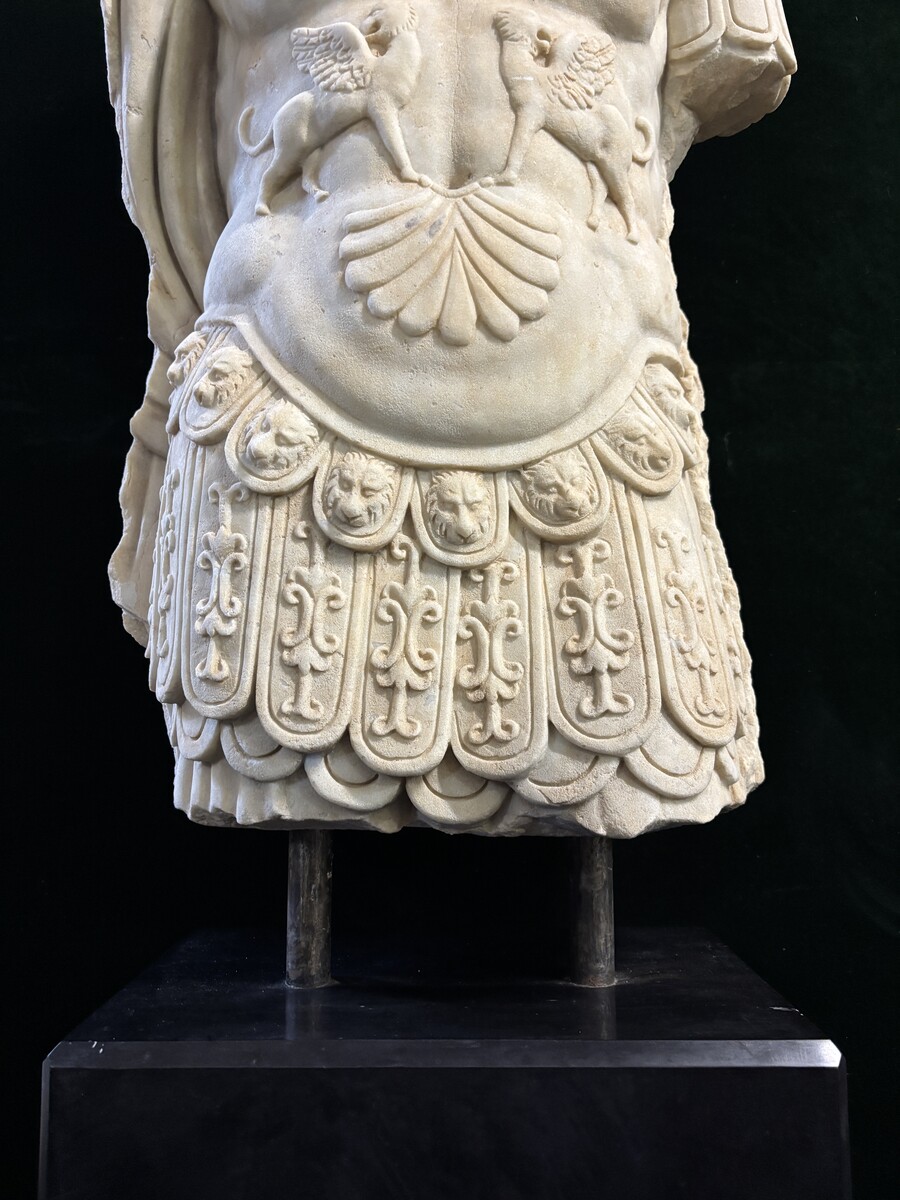 An impressive sculpture of a Roman torso in white marble, exuding the power and beauty of classical antiquity. The detailed breastplate is richly decorated with hand-carved mythological motifs. 