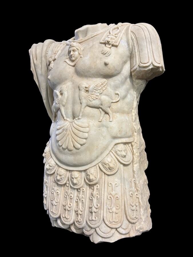 An impressive sculpture of a Roman torso in white marble, exuding the power and beauty of classical antiquity. The detailed breastplate is richly decorated with hand-carved mythological motifs. 
