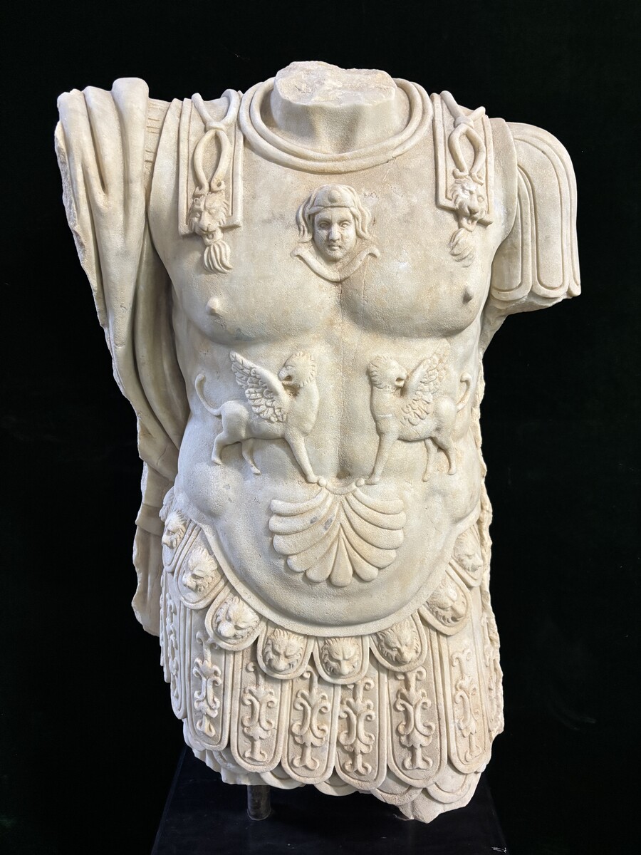 An impressive sculpture of a Roman torso in white marble, exuding the power and beauty of classical antiquity. The detailed breastplate is richly decorated with hand-carved mythological motifs. 