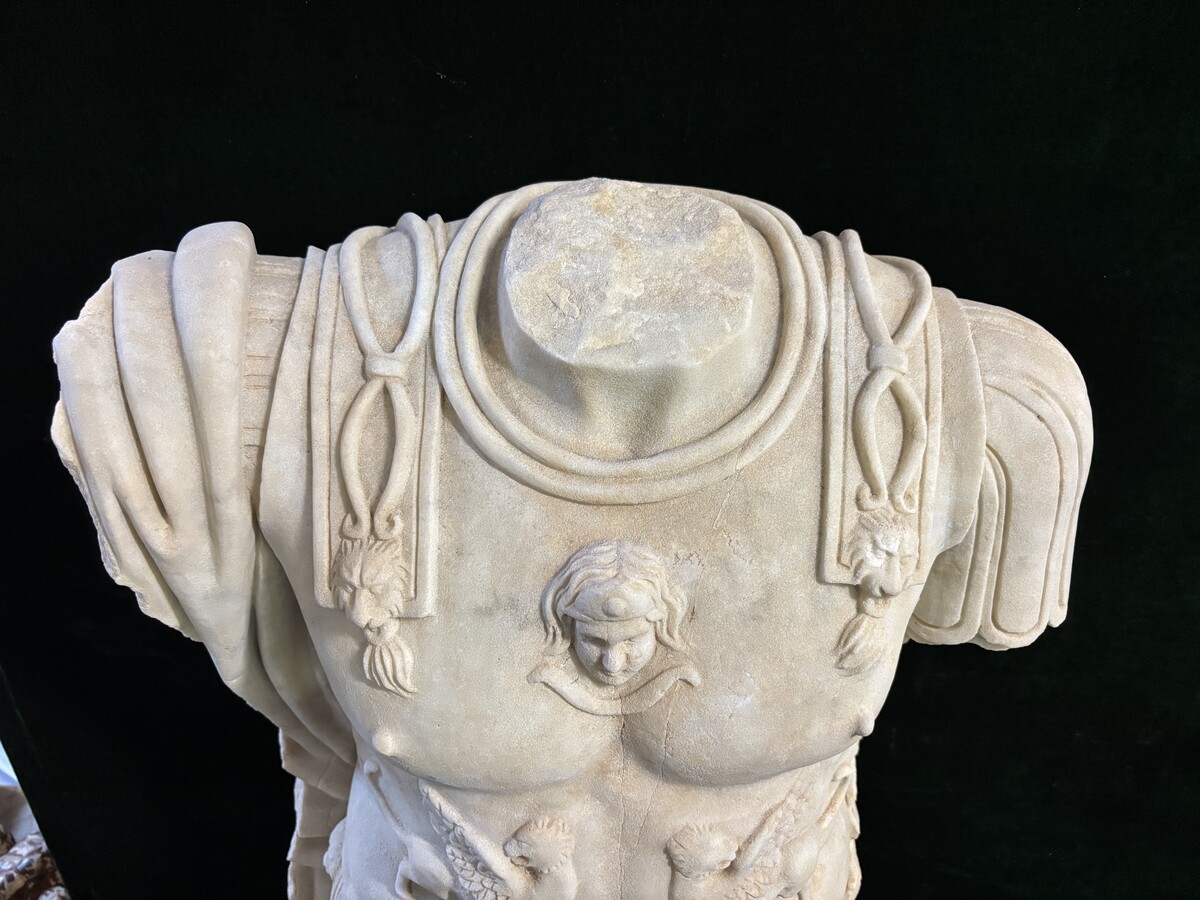 An impressive sculpture of a Roman torso in white marble, exuding the power and beauty of classical antiquity. The detailed breastplate is richly decorated with hand-carved mythological motifs. 