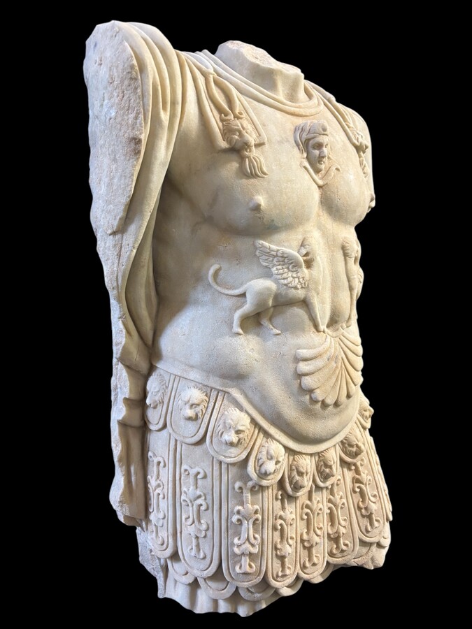 An impressive sculpture of a Roman torso in white marble, exuding the power and beauty of classical antiquity. The detailed breastplate is richly decorated with hand-carved mythological motifs. 