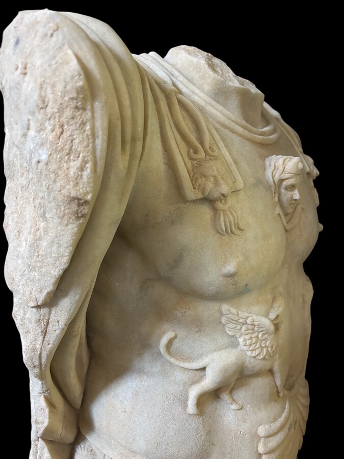 An impressive sculpture of a Roman torso in white marble, exuding the power and beauty of classical antiquity. The detailed breastplate is richly decorated with hand-carved mythological motifs. 