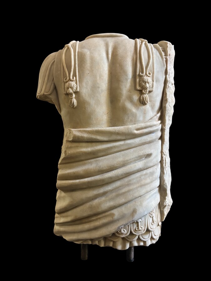 An impressive sculpture of a Roman torso in white marble, exuding the power and beauty of classical antiquity. The detailed breastplate is richly decorated with hand-carved mythological motifs. 