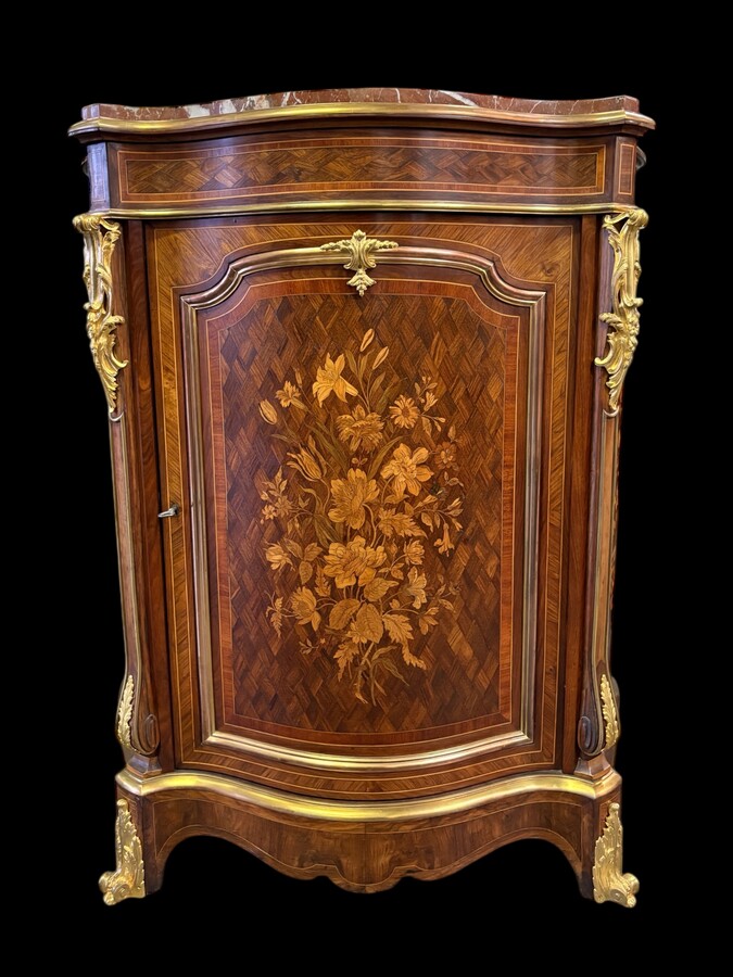 Attractive sideboard with a slightly curved front in rosewood veneer, rosewood and various precious woods. Central door and curved sides decorated with a floral bouquet, interior with two shelves, richly decorated with gilded bronze fittings. 