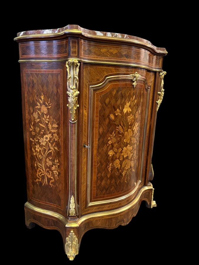 Attractive sideboard with a slightly curved front in rosewood veneer, rosewood and various precious woods. Central door and curved sides decorated with a floral bouquet, interior with two shelves, richly decorated with gilded bronze fittings. 