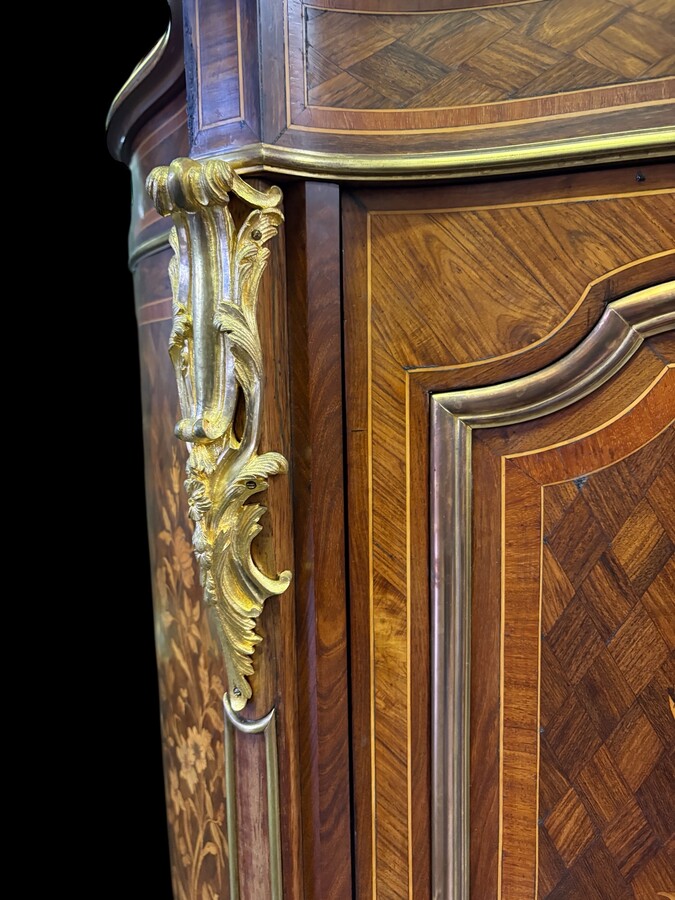 Attractive sideboard with a slightly curved front in rosewood veneer, rosewood and various precious woods. Central door and curved sides decorated with a floral bouquet, interior with two shelves, richly decorated with gilded bronze fittings. 