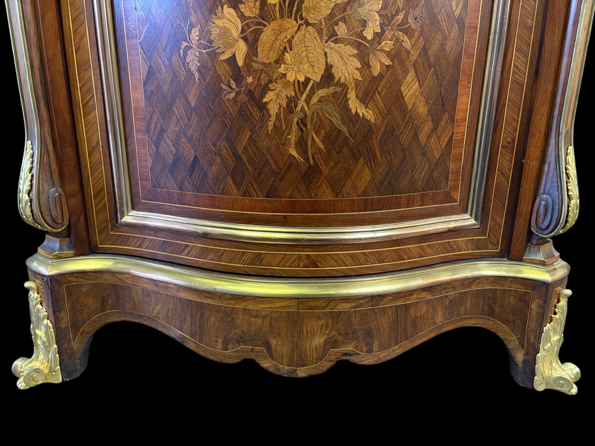 Attractive sideboard with a slightly curved front in rosewood veneer, rosewood and various precious woods. Central door and curved sides decorated with a floral bouquet, interior with two shelves, richly decorated with gilded bronze fittings. 