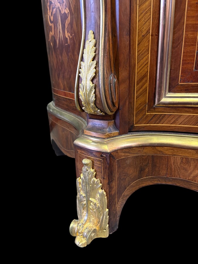 Attractive sideboard with a slightly curved front in rosewood veneer, rosewood and various precious woods. Central door and curved sides decorated with a floral bouquet, interior with two shelves, richly decorated with gilded bronze fittings. 