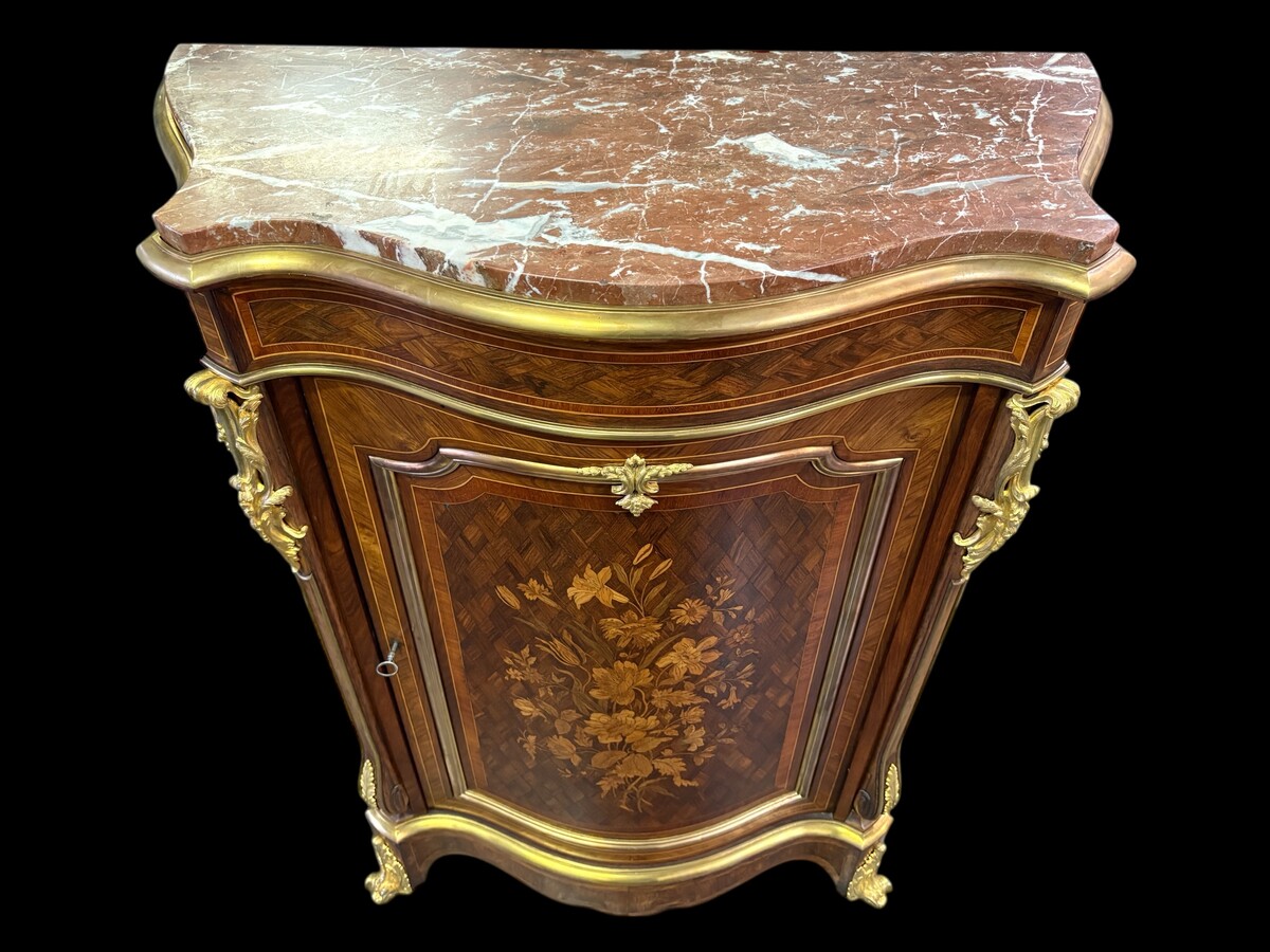 Attractive sideboard with a slightly curved front in rosewood veneer, rosewood and various precious woods. Central door and curved sides decorated with a floral bouquet, interior with two shelves, richly decorated with gilded bronze fittings. 