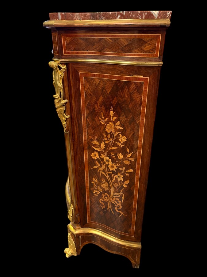 Attractive sideboard with a slightly curved front in rosewood veneer, rosewood and various precious woods. Central door and curved sides decorated with a floral bouquet, interior with two shelves, richly decorated with gilded bronze fittings. 