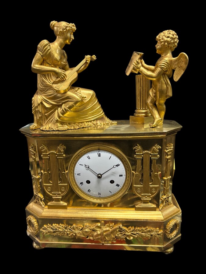 Beautiful Empire period clock in matt and bright gilt bronze depicting a lady playing guitar with an angel. In very good condition, the movement has not been checked. The balance wheel is present. Dimensions: Width: 31.5 cm Height: 43 cm Depth : 13 cm