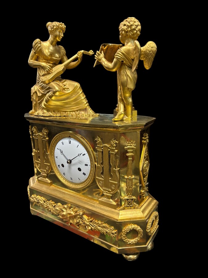 Beautiful Empire period clock in matt and bright gilt bronze depicting a lady playing guitar with an angel. In very good condition, the movement has not been checked. The balance wheel is present. Dimensions: Width: 31.5 cm Height: 43 cm Depth : 13 cm
