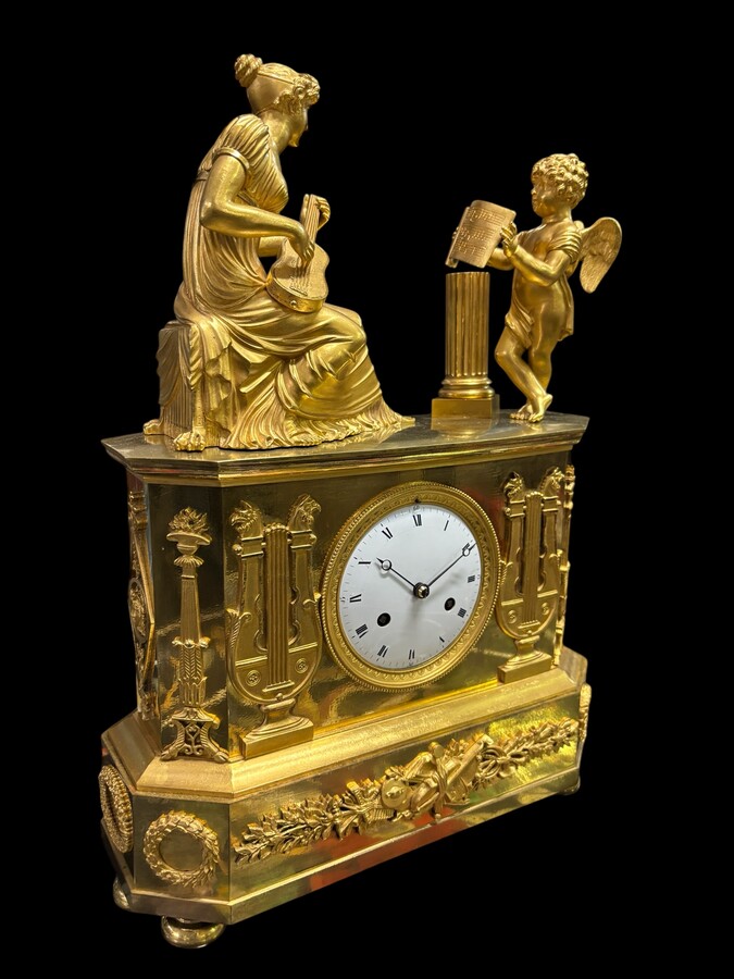 Beautiful Empire period clock in matt and bright gilt bronze depicting a lady playing guitar with an angel. In very good condition, the movement has not been checked. The balance wheel is present. Dimensions: Width: 31.5 cm Height: 43 cm Depth : 13 cm