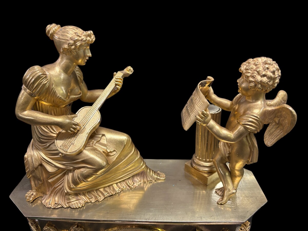 Beautiful Empire period clock in matt and bright gilt bronze depicting a lady playing guitar with an angel. In very good condition, the movement has not been checked. The balance wheel is present. Dimensions: Width: 31.5 cm Height: 43 cm Depth : 13 cm