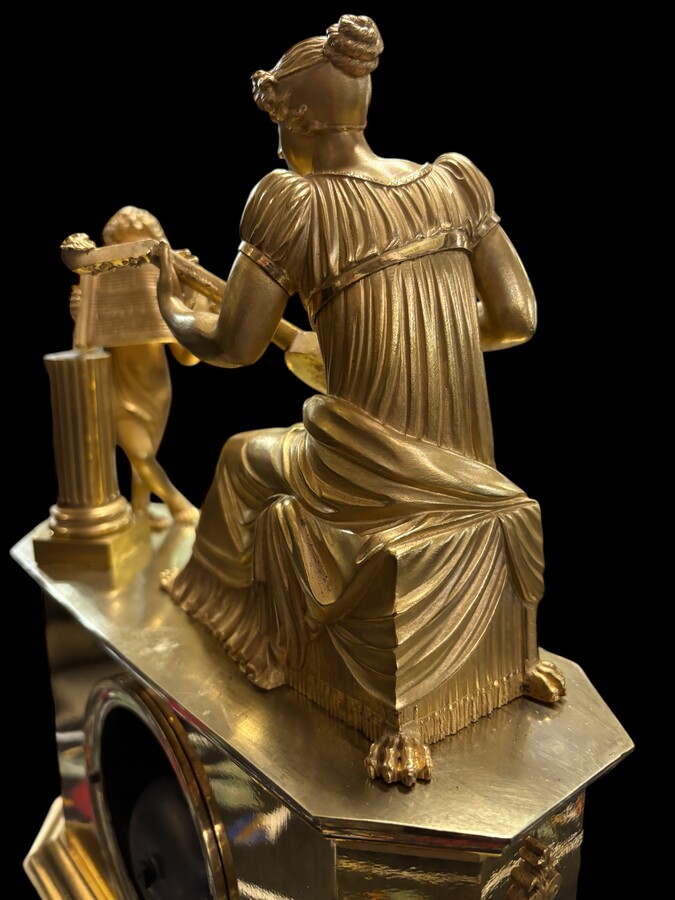 Beautiful Empire period clock in matt and bright gilt bronze depicting a lady playing guitar with an angel. In very good condition, the movement has not been checked. The balance wheel is present. Dimensions: Width: 31.5 cm Height: 43 cm Depth : 13 cm