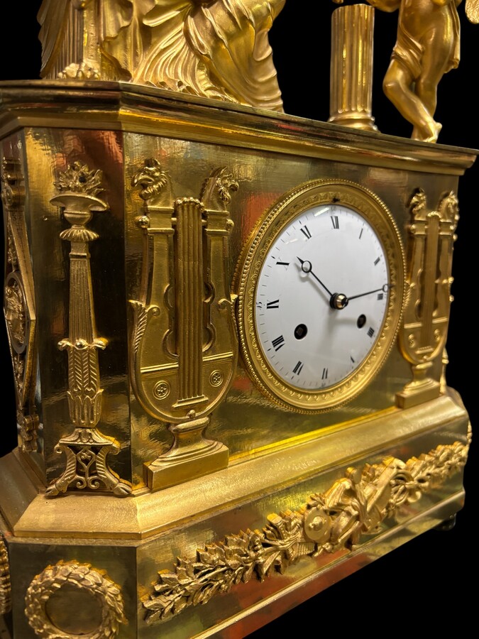 Beautiful Empire period clock in matt and bright gilt bronze depicting a lady playing guitar with an angel. In very good condition, the movement has not been checked. The balance wheel is present. Dimensions: Width: 31.5 cm Height: 43 cm Depth : 13 cm