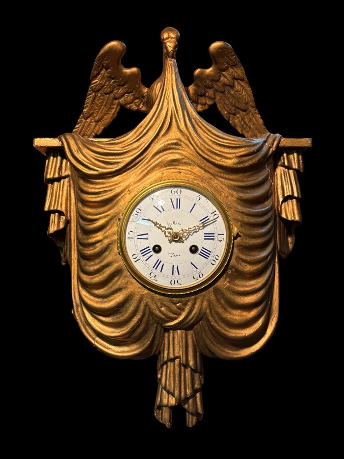 Elegant 19th-century gilt wooden eagle clock with drapery Decorative clock in gilt wood and paste depicting an eagle carrying a large drapery that falls to the left and right of the dial. In normal condition with a few small flaws on the wood.