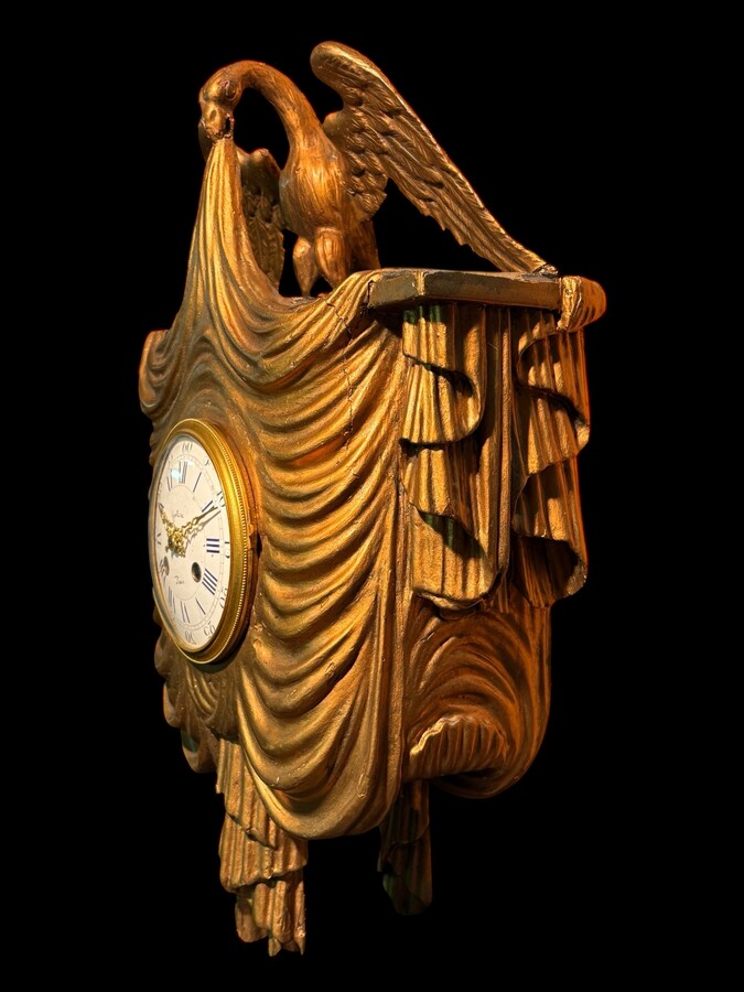 Elegant 19th-century gilt wooden eagle clock with drapery Decorative clock in gilt wood and paste depicting an eagle carrying a large drapery that falls to the left and right of the dial. In normal condition with a few small flaws on the wood.