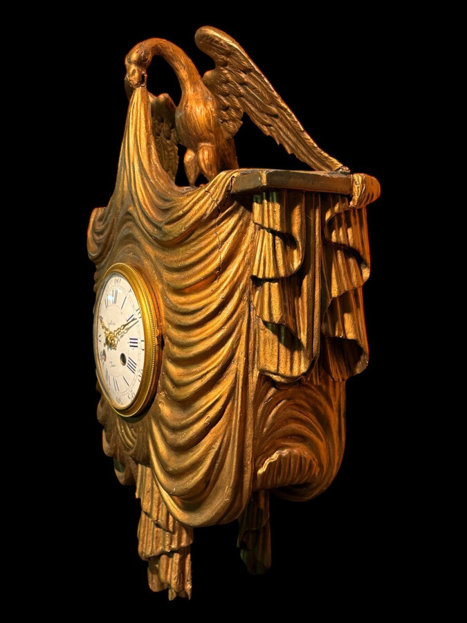 Elegant 19th-century gilt wooden eagle clock with drapery Decorative clock in gilt wood and paste depicting an eagle carrying a large drapery that falls to the left and right of the dial. In normal condition with a few small flaws on the wood.