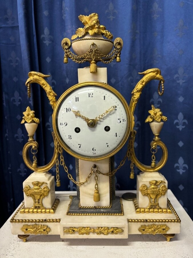Elegant Louis XVI style clock from the 18th century. Beautiful 18th century marble and gilt bronze mantel clock decorated with vases of flowers, ornaments, griffin heads and bronze girlandes. The pendulum and key are present. 18thC.