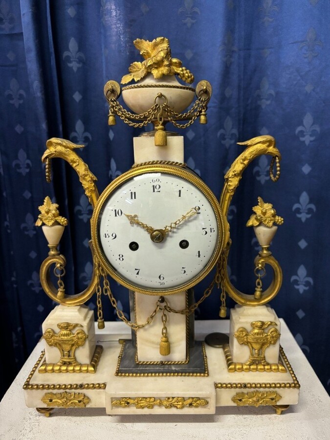 Elegant Louis XVI style clock from the 18th century. Beautiful 18th century marble and gilt bronze mantel clock decorated with vases of flowers, ornaments, griffin heads and bronze girlandes. The pendulum and key are present. 18thC.