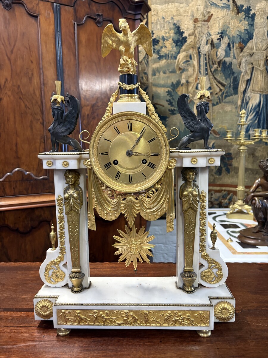 Large Empire-style portico clock (64.5 cm), 19thC. Large clock featuring two marble columns adorned with two caryatids, rosettes, drapery, decorative motifs, two patinated and gilded sphinxes, and an eagle at the top. Sun dial and key included; move