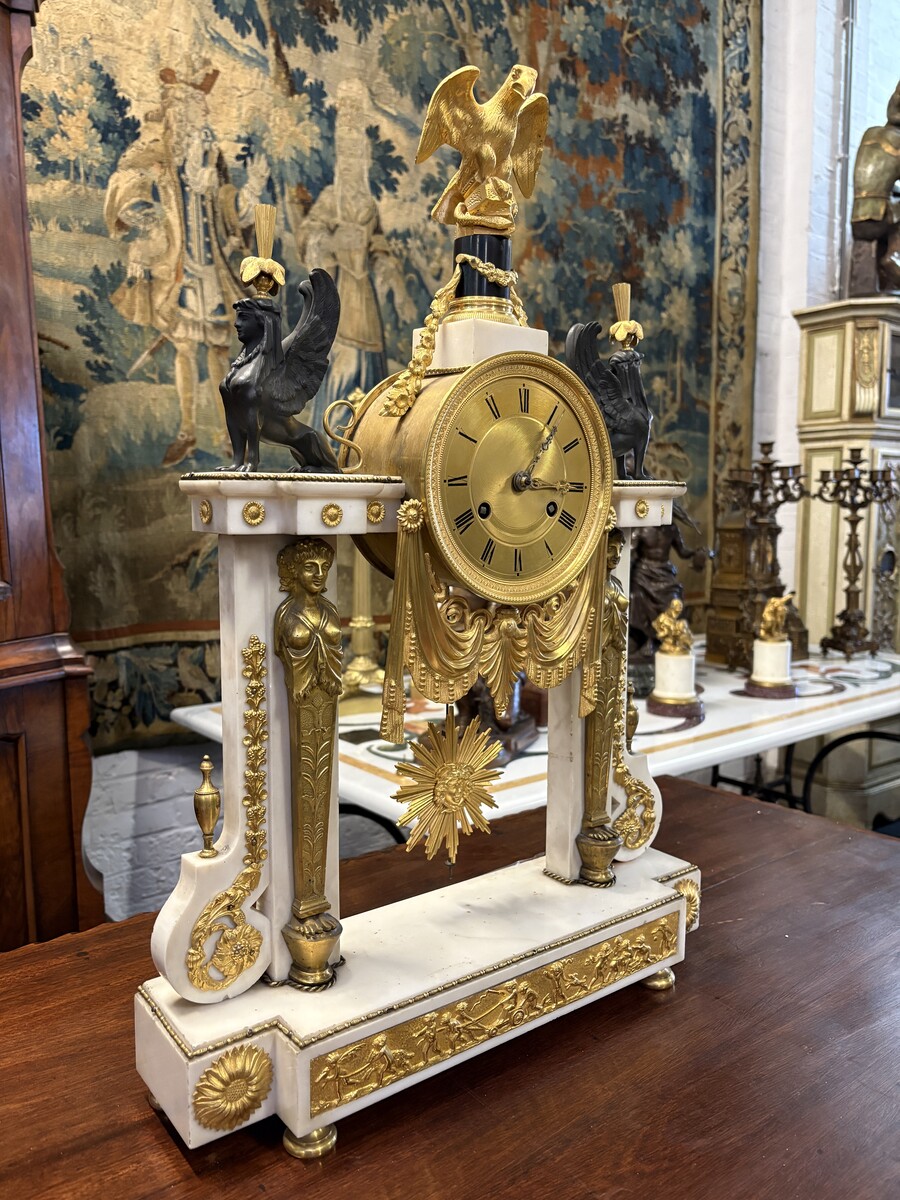Large Empire-style portico clock (64.5 cm), 19thC. Large clock featuring two marble columns adorned with two caryatids, rosettes, drapery, decorative motifs, two patinated and gilded sphinxes, and an eagle at the top. Sun dial and key included; move