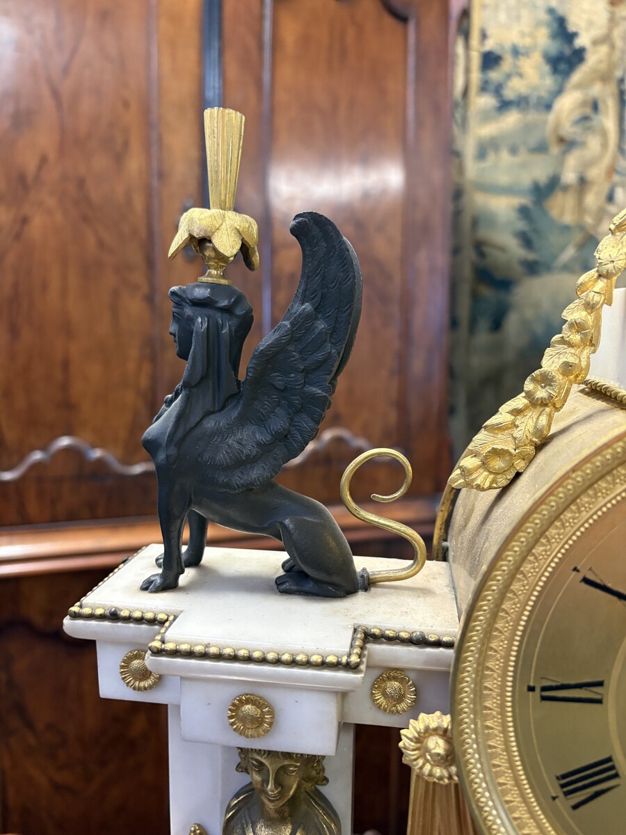 Large Empire-style portico clock (64.5 cm), 19thC. Large clock featuring two marble columns adorned with two caryatids, rosettes, drapery, decorative motifs, two patinated and gilded sphinxes, and an eagle at the top. Sun dial and key included; move