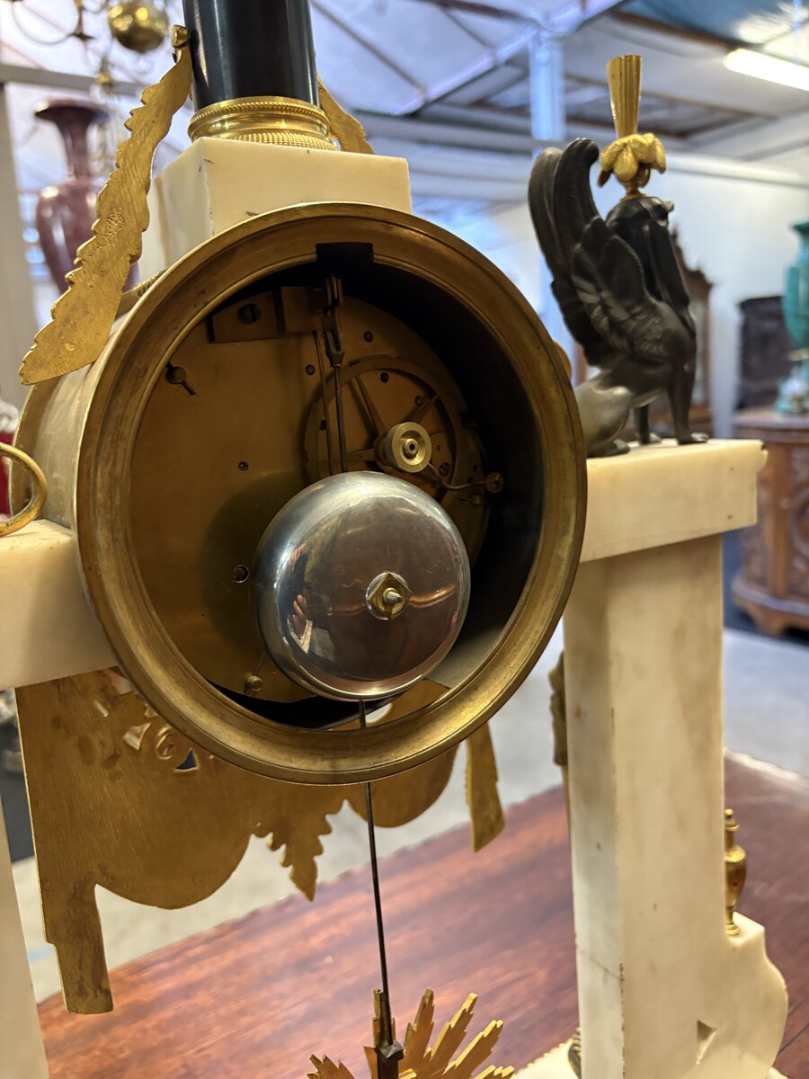 Large Empire-style portico clock (64.5 cm), 19thC. Large clock featuring two marble columns adorned with two caryatids, rosettes, drapery, decorative motifs, two patinated and gilded sphinxes, and an eagle at the top. Sun dial and key included; move