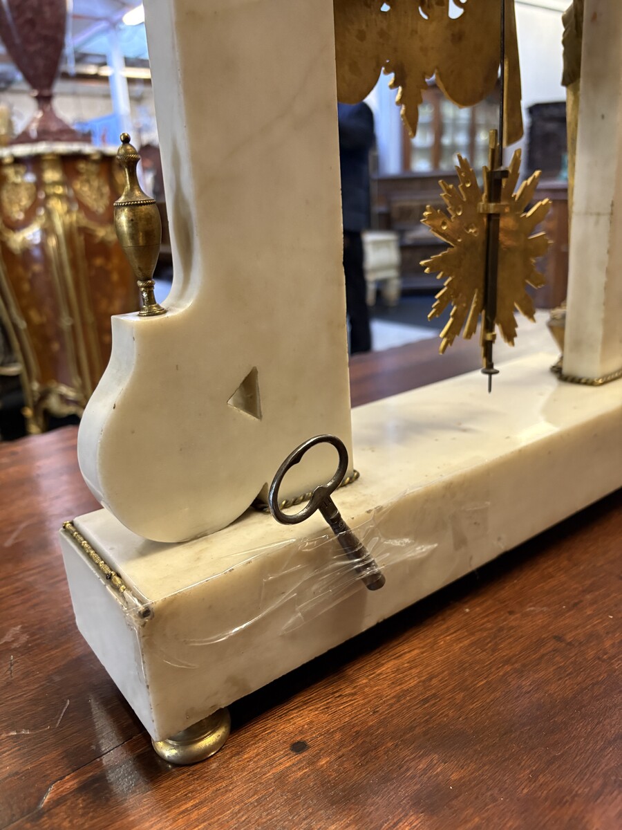 Large Empire-style portico clock (64.5 cm), 19thC. Large clock featuring two marble columns adorned with two caryatids, rosettes, drapery, decorative motifs, two patinated and gilded sphinxes, and an eagle at the top. Sun dial and key included; move