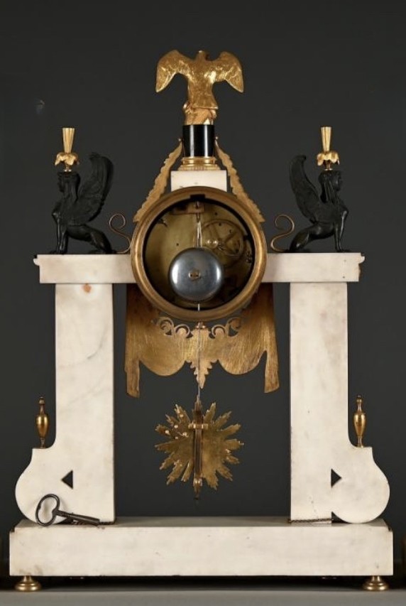 Large Empire-style portico clock (64.5 cm), 19thC. Large clock featuring two marble columns adorned with two caryatids, rosettes, drapery, decorative motifs, two patinated and gilded sphinxes, and an eagle at the top. Sun dial and key included; move