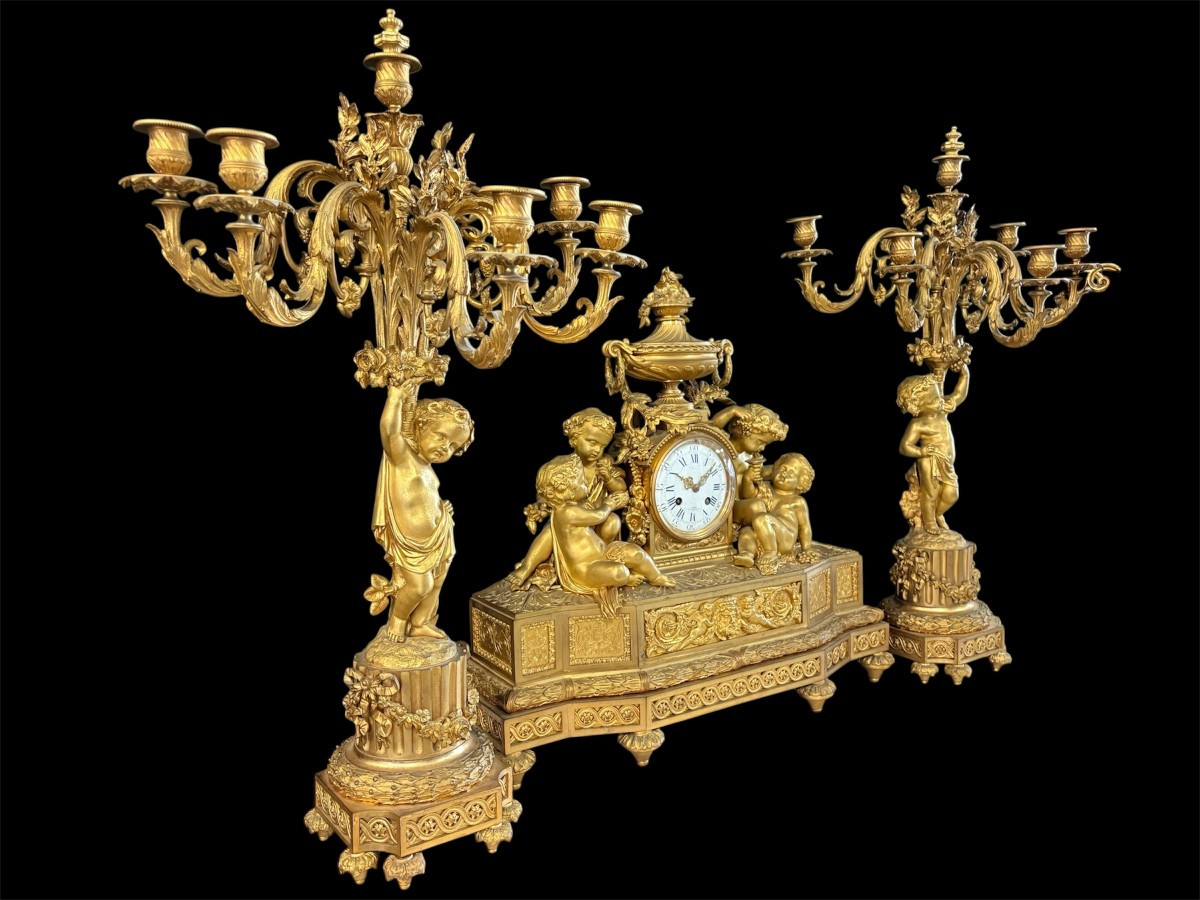 Large gilt bronze clock set. Paris, 19th century. A beautiful large clock with four cherubs and very fine gilt bronze decorations, as well as two candlesticks representing two large cherubs carrying a torch with six candlesticks.